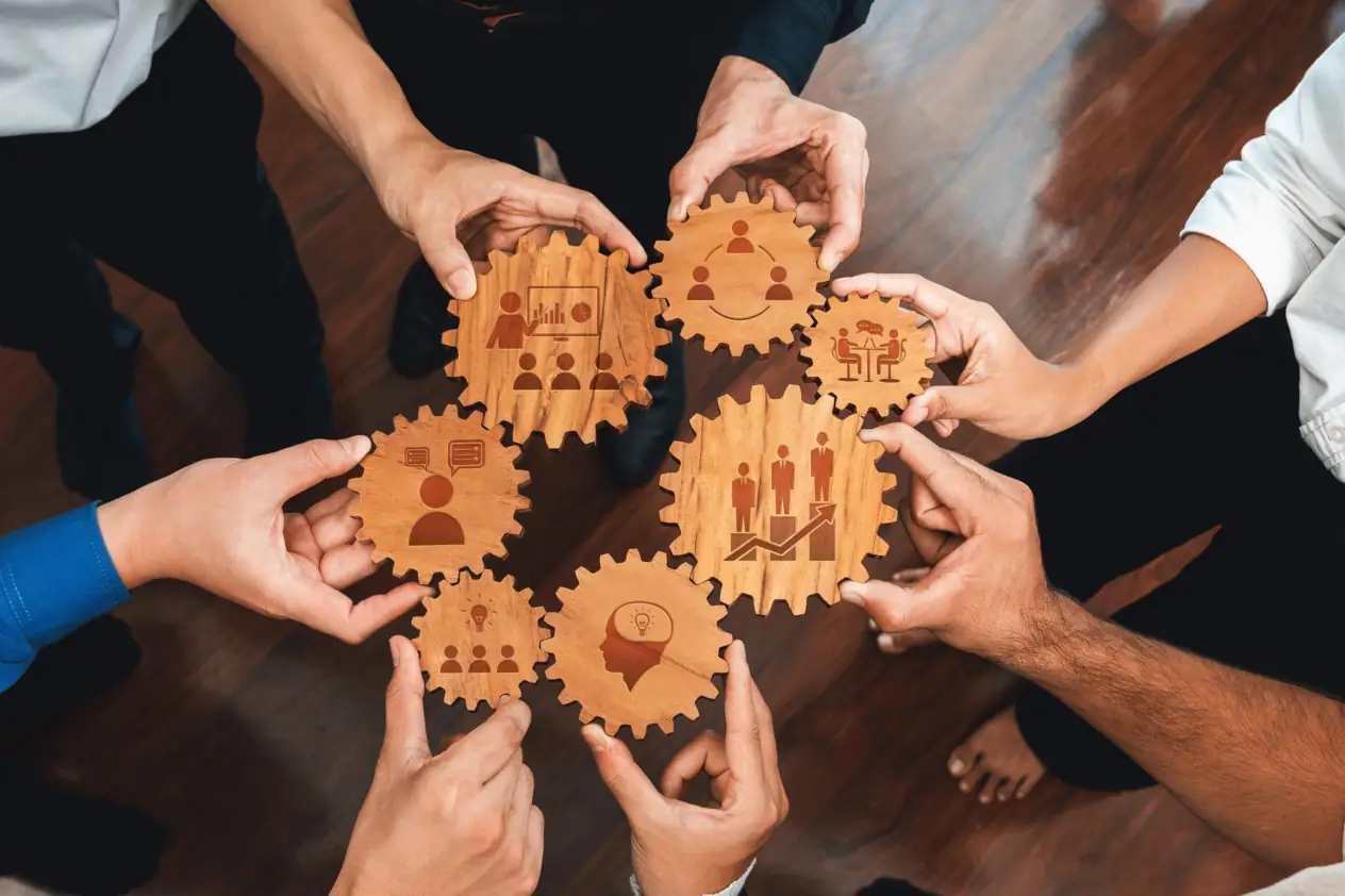Diverse hands holding interlocking wooden gears, symbolizing teamwork and collaboration essential for success in modern business settings.